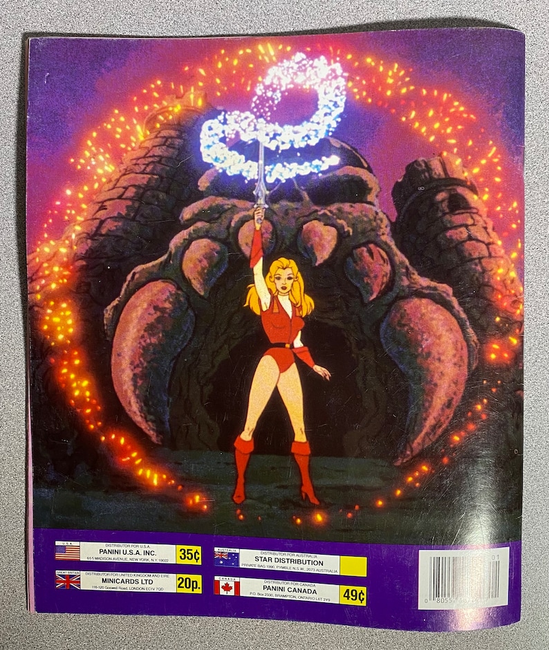 Może przedstawiać: Vintage naklejka Panini z kresk&oacute;wkową ilustracją wojowniczki w czerwonym stroju, trzymającej miecz w g&oacute;rze. Stoi przed dużą konstrukcją z efektem świecącej energii. Naklejka ma tekst na dole.