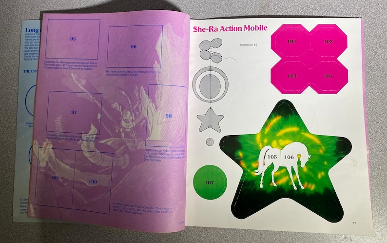 Może przedstawiać: Otwarta książka ze stronami z ilustracją She-Ra Action Mobile. Ilustracja zawiera naklejkę w kształcie gwiazdy z białą sylwetką konia, r&oacute;żowe kształty i zielone koło. Obecne są r&oacute;wnież ponumerowane pola i tekst.