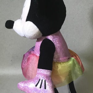 May include: A pink and black plush Minnie Mouse doll wearing a sparkly pink dress with a rainbow tulle skirt and pink shoes.