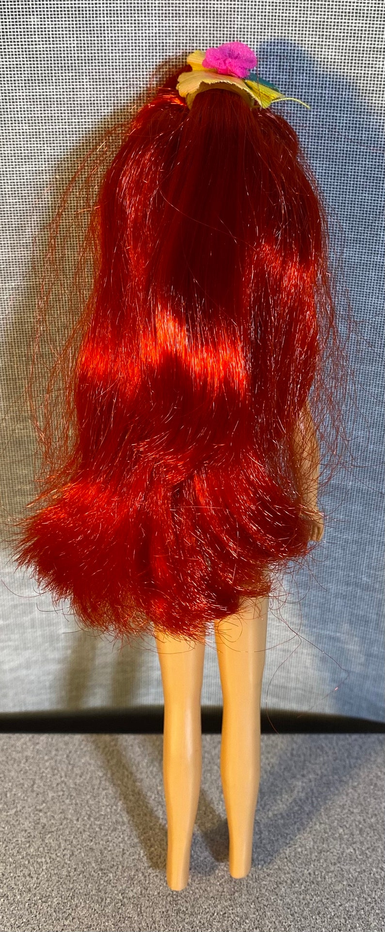 Pu&ograve; includere: Una bambola con i capelli rossi e un fiore tra i capelli. La bambola indossa un costume da bagno e ha un'abbronzatura.