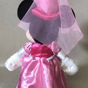 K&ouml;nnte beinhalten: Eine rosafarbene und wei&szlig;e Pl&uuml;sch-Minnie-Maus-Puppe, die ein rosafarbenes Kleid und einen rosafarbenen T&uuml;llschleier tr&auml;gt.