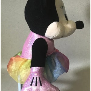 May include: A pink and black plush toy of Minnie Mouse wearing a pink sparkly dress with a rainbow tulle skirt and pink sparkly shoes.