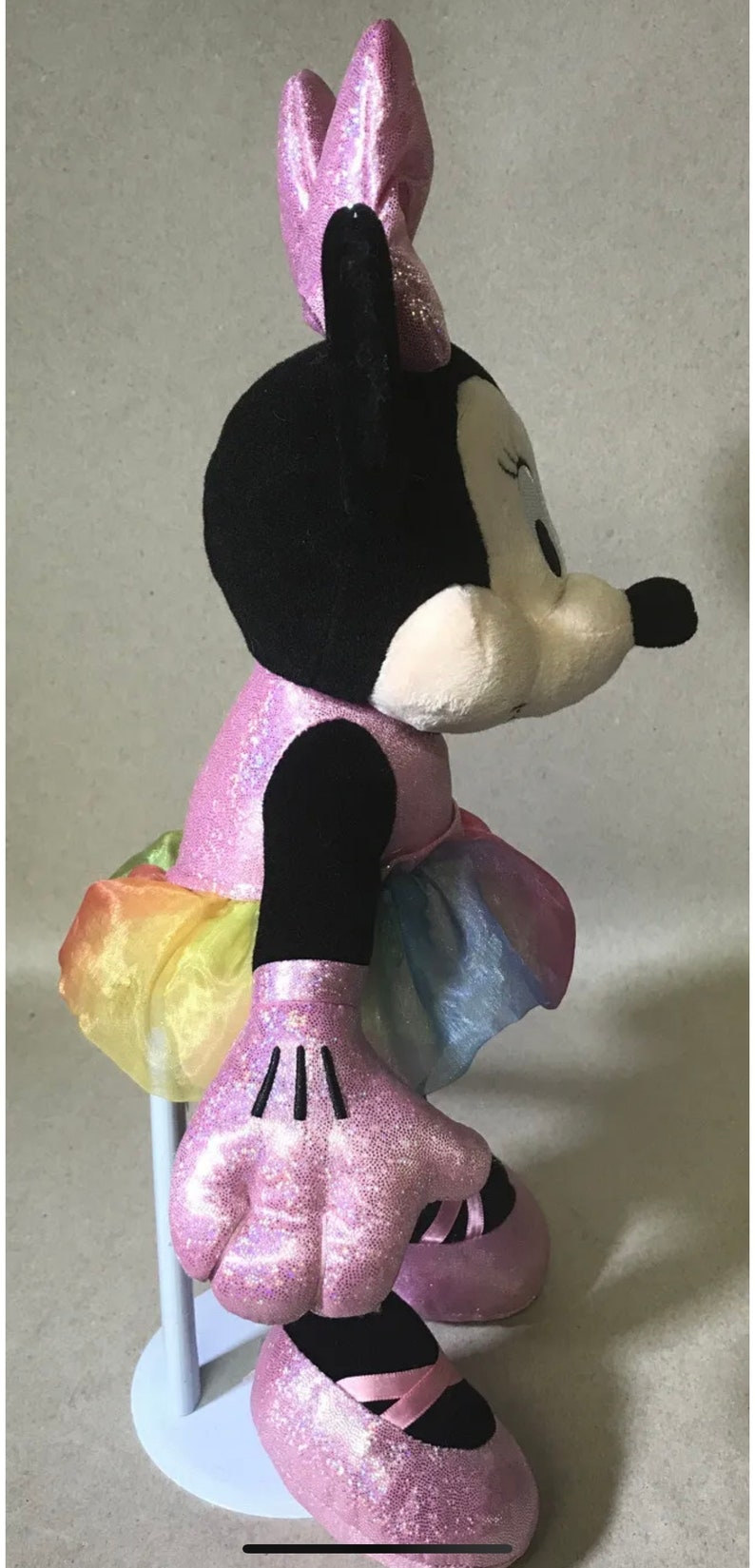 May include: A pink and black plush toy of Minnie Mouse wearing a pink sparkly dress with a rainbow tulle skirt and pink sparkly shoes.