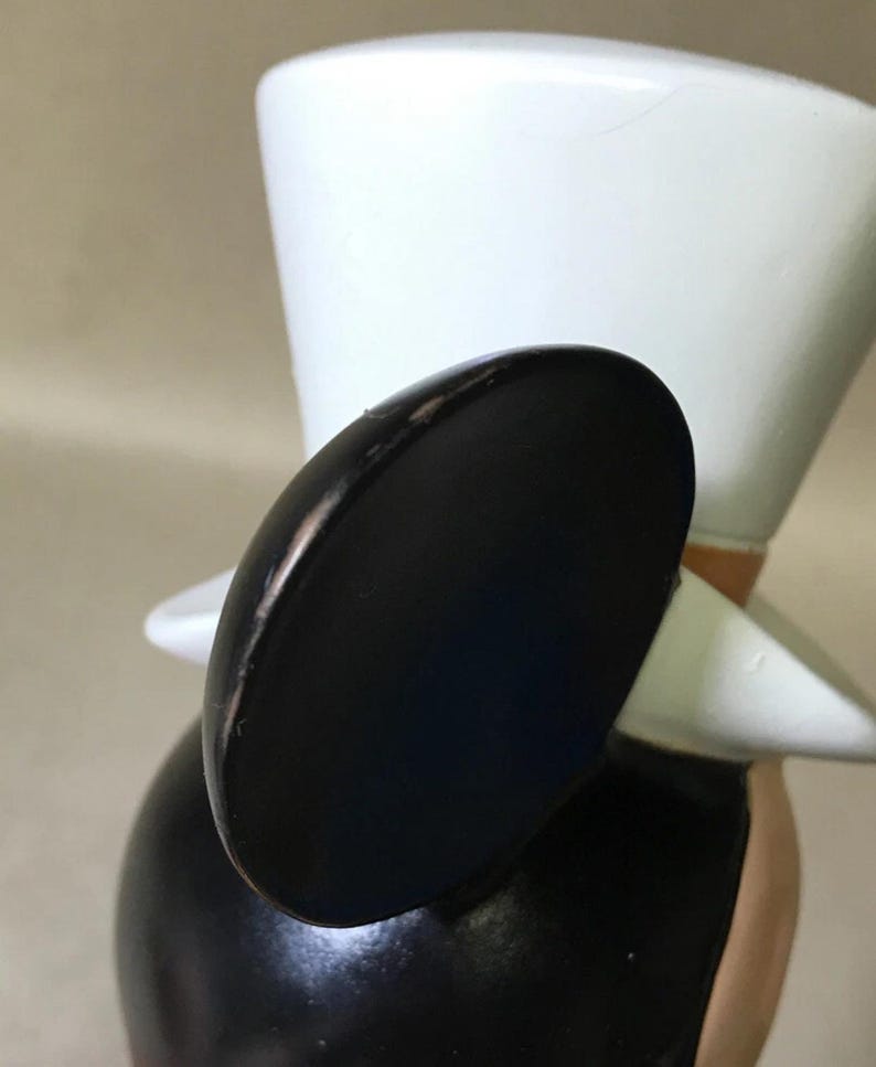 May include: A black and white figurine of a cartoon character wearing a top hat. The figurine has large black ears, a white hat, and a black body. The character's face is not visible in the image.