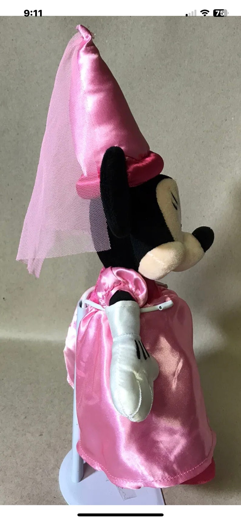 K&ouml;nnte beinhalten: Ein rosa Pl&uuml;sch-Minnie Mouse, verkleidet als Prinzessin. Sie tr&auml;gt ein rosa Kleid, eine rosa Krone und einen wei&szlig;en Schleier. Sie steht auf einem wei&szlig;en Sockel.