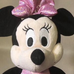 May include: A plush toy of Minnie Mouse with a pink sparkly bow. She has black ears, a white face, and black eyes with white eyelashes.