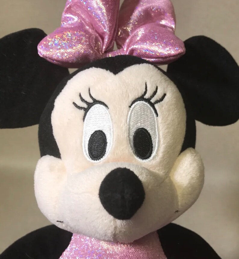May include: A plush toy of Minnie Mouse with a pink sparkly bow. She has black ears, a white face, and black eyes with white eyelashes.