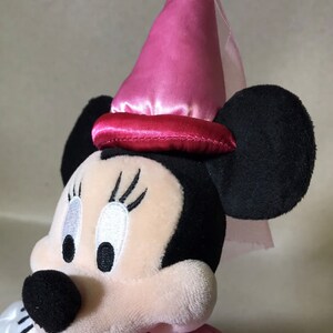 K&ouml;nnte beinhalten: Ein rosa-schwarzes Pl&uuml;schtier von Minnie Mouse, das einen rosa Satin-Hut mit Schleier tr&auml;gt. Der Hut hat ein rotes Satinband um die Basis.