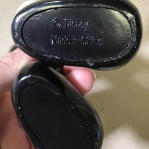 May include: Close-up of the black base of a Disney figurine. The text "&copy; Disney Made in China" is embossed on the base. The figurine's base is oval-shaped and has a glossy finish.