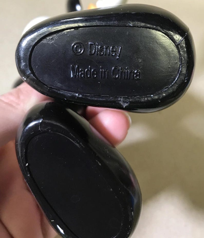 May include: Close-up of the black base of a Disney figurine. The text "&copy; Disney Made in China" is embossed on the base. The figurine's base is oval-shaped and has a glossy finish.