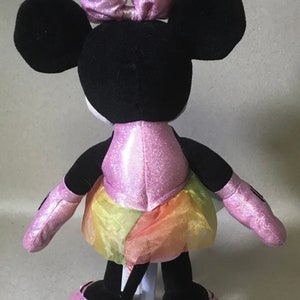 May include: A pink and black plush Minnie Mouse toy wearing a pink sparkly dress and a pink bow. The dress has a rainbow tulle skirt.