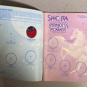 Może przedstawiać: Otwarty album z naklejkami She-Ra: Princess of Power. Lewa strona zawiera tekst i opisy postaci, a prawa ilustracje postaci. Okładka przedstawia logo She-Ra i jednorożca. Nostalgiczny przedmiot kolekcjonerski.