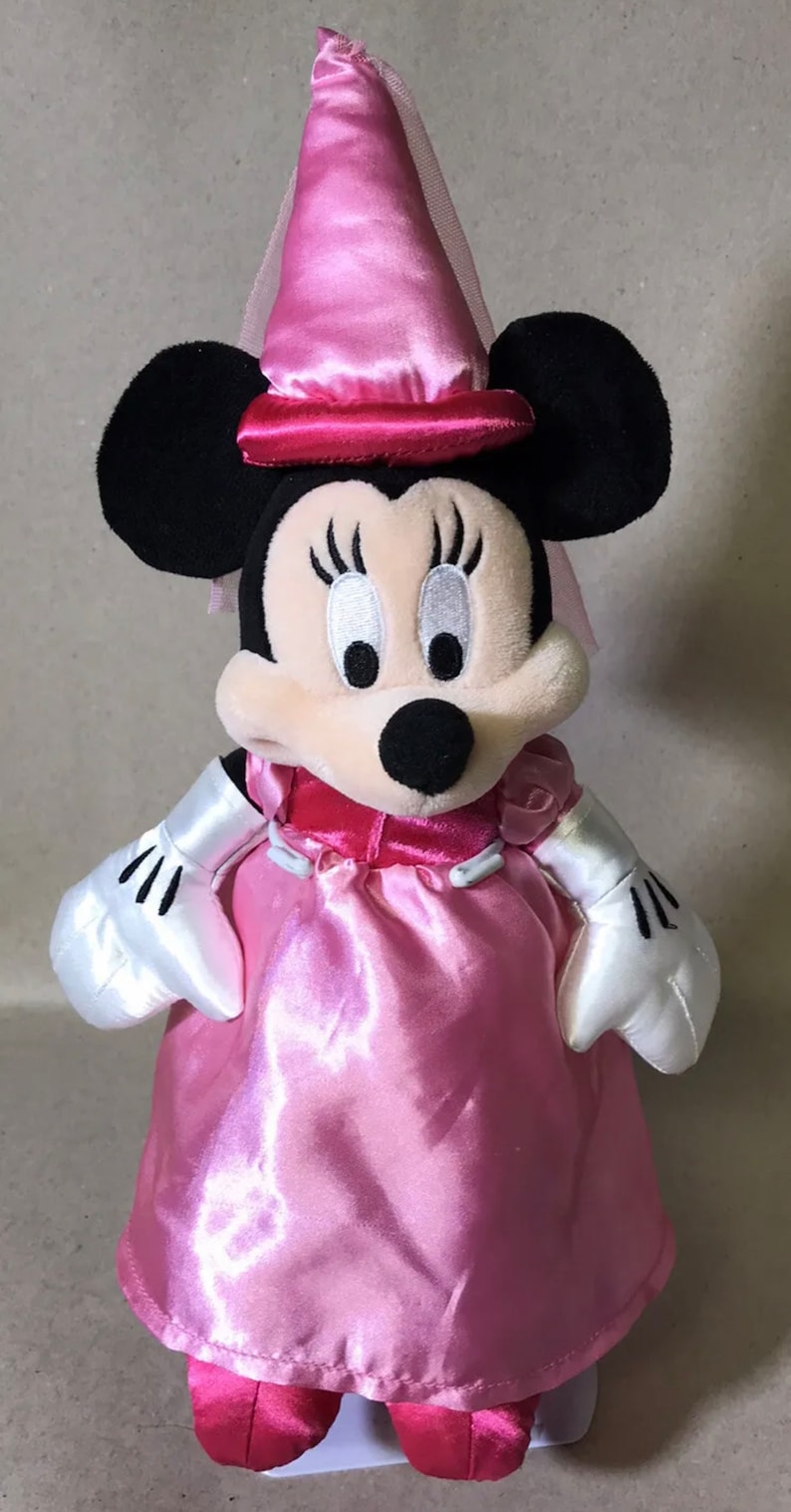 K&ouml;nnte beinhalten: Ein rosa Pl&uuml;sch-Minnie Mouse, verkleidet als Prinzessin. Sie tr&auml;gt ein rosa Kleid mit wei&szlig;em Satinbesatz, eine rosa Krone mit wei&szlig;em Schleier und rosa Schuhe.