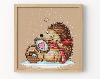 Op de afbeelding: Een bruine egel met een rode sjaal houdt een hoepel vast met een roze hart erin. De egel zit op een besneeuwde grond met een mand vol kleurrijke spullen ernaast. Er zijn kleine witte stippen op de achtergrond.
