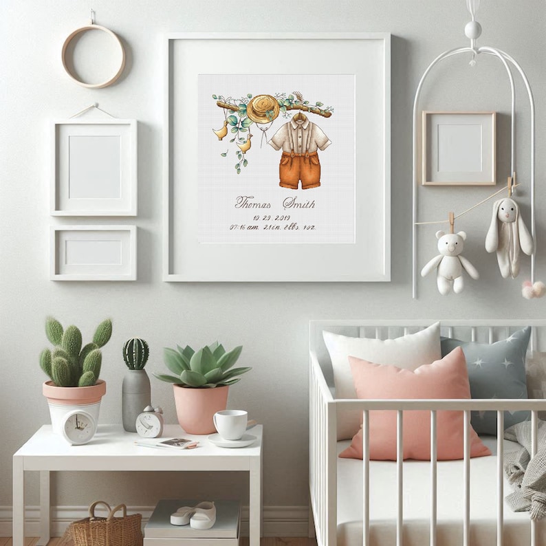 Op de afbeelding: Een ingelijste aquarelprint met een babyoutfit, hoed en bloemaccenten. De print bevat de naam "Thomas Smith" en geboortegegevens. De kinderkamerdecoratie omvat ook een witte wieg, knuffels en potplanten.