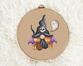 Op de afbeelding: Een borduurring met een kruissteekpatroon met een Halloween-thema. Een kabouter met een heksenhoed en een bezem in de hand wordt omringd door pompoenen en een spook.