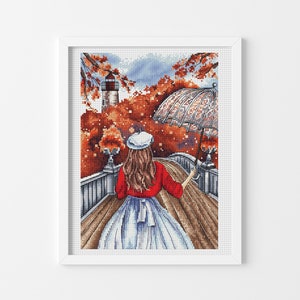 Puede incluir: Una mujer con un suéter rojo y una falda blanca camina por un puente con una boina blanca y una sombrilla blanca. El puente está rodeado de follaje otoñal y se puede ver un faro en el fondo.