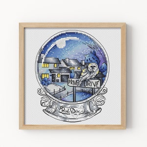 Op de afbeelding: Een besneeuwde nachtscène met een huis en een bord met de tekst "Privet Drive" in een glazen sneeuwbol. Twee uilen zitten op het bord. De sneeuwbol is omgeven door een decoratief frame.
