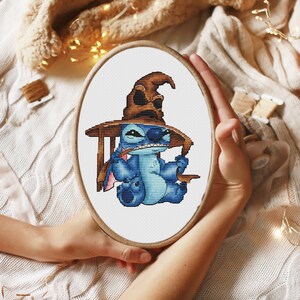 K&ouml;nnte beinhalten: Eine blaue Stitch-Figur, die einen braunen Sortierhut aus der Harry-Potter-Reihe tr&auml;gt. Die Figur sitzt auf einem Holzstuhl und h&auml;lt einen Zauberstab.