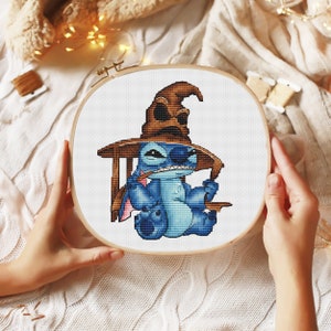 K&ouml;nnte beinhalten: Eine blaue Stitch-Figur, die einen braunen Sortierhut aus der Harry-Potter-Reihe tr&auml;gt. Die Figur sitzt auf einem Stuhl und h&auml;lt einen Zauberstab.