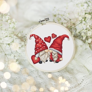 May include: Cross-stitch pattern of two gnomes kissing with red hearts around them. The gnomes are wearing red hats with white polka dots and white beards.