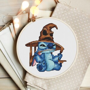 K&ouml;nnte beinhalten: Eine blaue Stitch-Figur, die einen braunen Sortierhut aus der Harry-Potter-Reihe tr&auml;gt. Die Figur sitzt auf einem Holzstuhl mit einem Zauberstab in der Hand.