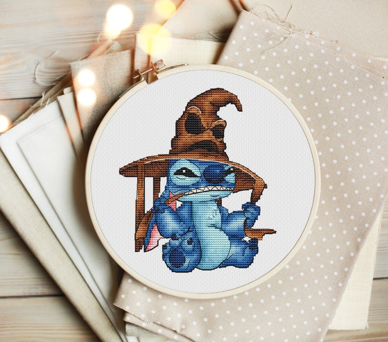 K&ouml;nnte beinhalten: Eine blaue Stitch-Figur, die einen braunen Sortierhut aus der Harry-Potter-Reihe tr&auml;gt. Die Figur sitzt auf einem Holzstuhl mit einem Zauberstab in der Hand.