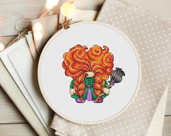 May include: Cross-stitch pattern of a red-haired witch holding a black broom. The witch is wearing a green dress with a purple bodice and has a braided hairstyle.