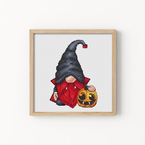 May include: A cross-stitch pattern of a gnome dressed as a vampire holding a jack-o'-lantern. The gnome is wearing a black hat, red cape, and has a white beard. The jack-o'-lantern is orange with a black face.