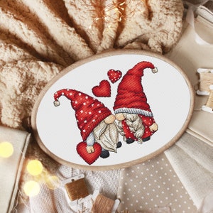 May include: Cross-stitch pattern of two gnomes holding red hearts, surrounded by smaller hearts. The gnomes are wearing red hats with white polka dots and white beards.