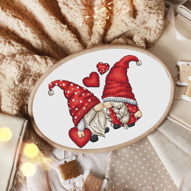May include: Cross-stitch pattern of two gnomes holding red hearts, surrounded by smaller hearts. The gnomes are wearing red hats with white polka dots and white beards.