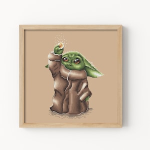 Puede incluir: Un patrón de punto de cruz de un personaje alienígena verde con ojos grandes, que lleva una túnica marrón y sostiene un pequeño objeto redondo en su mano derecha. El personaje está de pie sobre un fondo beige.