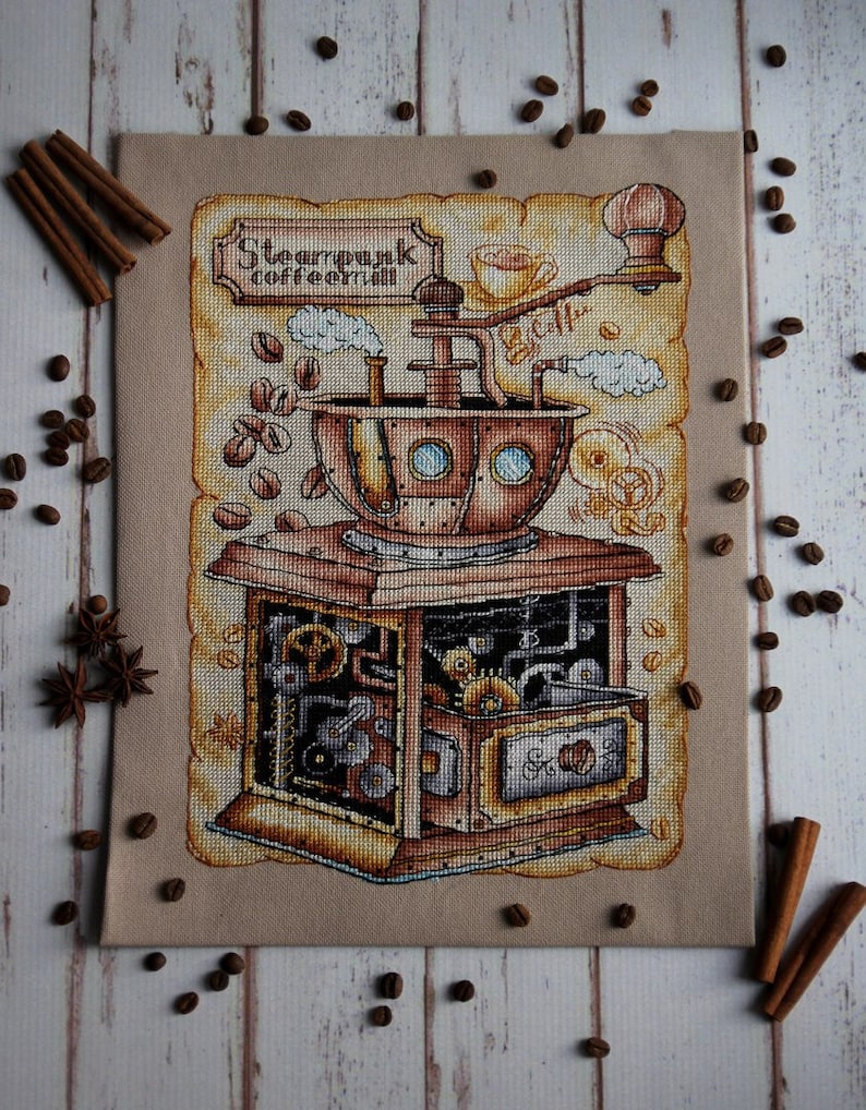 Op de afbeelding: Een kruissteekborduursel van een steampunk-koffiemaler met ingewikkelde tandwielen en pijpen. De maler is van metaal en heeft een houten basis. De tekst "Steampunk Coffee" staat op een bord boven de maler.