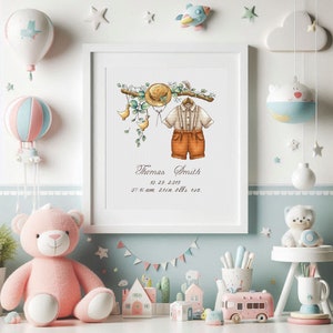 Op de afbeelding: Een ingelijste aquarelprint met babykleding, een strohoed en bloemaccenten. De print bevat de naam "Thomas Smith" en geboortedetails. De kinderkamerdecoratie is omgeven door een roze teddybeer, speelgoedhuisjes en een heteluchtballon.