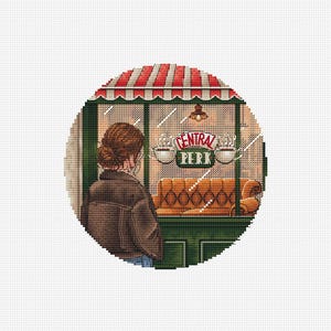 May include: A circular cross-stitch pattern depicting a person with brown hair in a bun wearing a dark jacket, standing before a storefront with a red and white striped awning. The window displays the text Central Perk with two coffee cups.