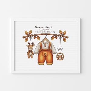 May include: A cross-stitch birth announcement featuring a white frame, orange overalls, a deer plush, and a bear rattle hanging from an oak branch. Text reads: Thomas Smith, 10.29.2019, 07:15 am, 21 in, 8 lbs, 4 oz. The design uses warm autumn colors.