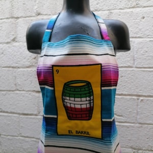 Puede incluir: Un delantal de cocina colorido con un diseño a rayas. El delantal presenta una carta de Loteria con la imagen de un barril y el texto "El Barril" y el número "9".