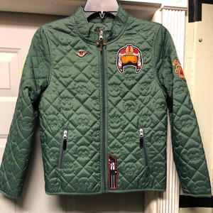 May include: A green quilted jacket with a Star Wars theme. It features a variety of patches, including a pilot helmet, a Rebel Alliance symbol, and a Stormtrooper.
