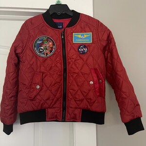 May include: Red quilted bomber jacket with black trim and multiple patches, including a NASA patch, a Commander patch, and a Teenage Mutant Ninja Turtles patch.