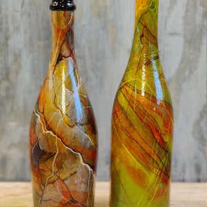 Pu&ograve; includere: Due bottiglie di vetro con disegni astratti colorati. Una bottiglia ha un design marmoreo marrone, arancione e bianco. L'altra bottiglia ha un design verde, giallo e arancione con linee sottili.