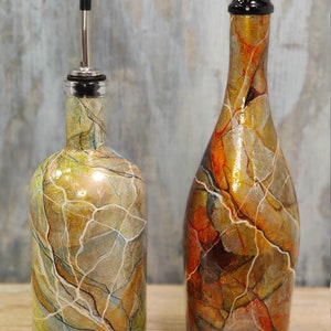 Pu&ograve; includere: Due bottiglie di vetro con vernice marmorizzata decorativa in tonalit&agrave; di marrone, oro e bianco. Le bottiglie hanno un beccuccio e un tappo.