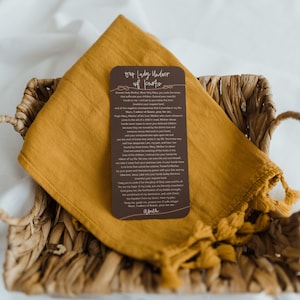 May include: A brown card with a prayer to Our Lady Undoer of Knots. The card features a decorative knot design and the text "Our Lady Undoer of Knots" in a light brown font. The prayer is written in a smaller font and includes the phrase "Mary, Undoer of Knots, pray for me."