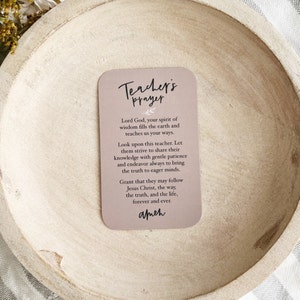 May include: A light brown card with the text "Teacher's Prayer" in a decorative font. The card features a prayer for teachers, asking for wisdom and guidance for them and their students. The prayer ends with the word "amen".