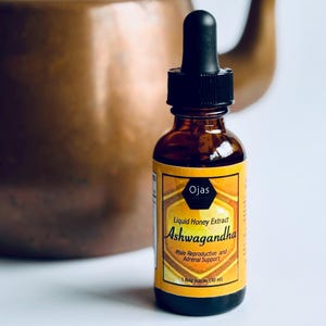 May include: A brown glass bottle with a black dropper top and a yellow label that reads "Ojas Liquid Honey Extract Ashwagandha Male Reproductive and Adrenal Support 1 fluid ounces (30 ml)"