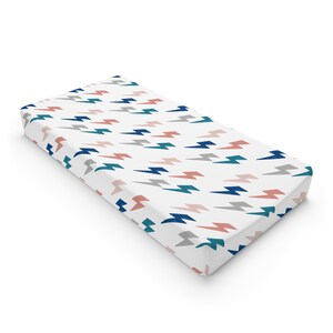 May include: A white fitted crib sheet with a lightning bolt pattern in shades of blue, teal, and pink.