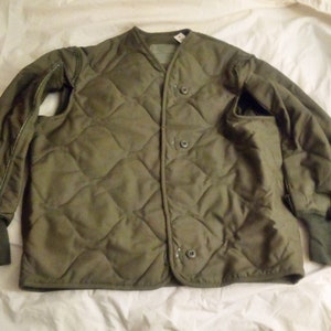 May include: A green quilted jacket with a snap closure and ribbed cuffs. The jacket has a diamond pattern and a pocket on the left side.