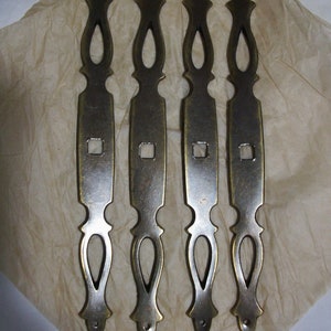 May include: Four antique brass drawer pulls with ornate designs. Each pull has a rectangular center with a square cutout and a decorative top and bottom.