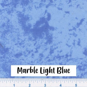 May include: A close-up of a light blue fabric with a marbled pattern. The fabric has a subtle texture and a light blue color with darker blue marbling. The text "Marble Light Blue" is printed on a white label below the fabric.