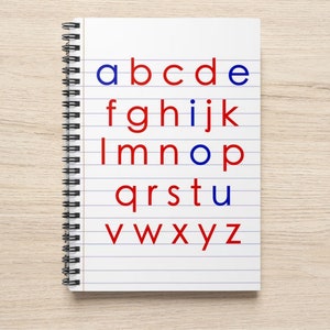 Pode incluir: Um caderno branco com letras azuis e vermelhas que soletram o alfabeto. As letras estão escritas em papel pautado em um caderno espiral.