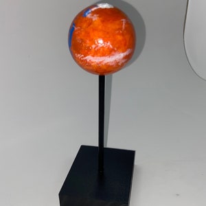Puede incluir: Un peque&ntilde;o globo naranja y blanco sobre un soporte negro. El globo est&aacute; pintado para parecerse a Marte.